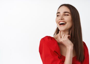 Close up portrait of attractive young woman in red dress, evening make up, laughing and smiling happy, enjoying party, looking aside at logo banner, read promo text, white background.
