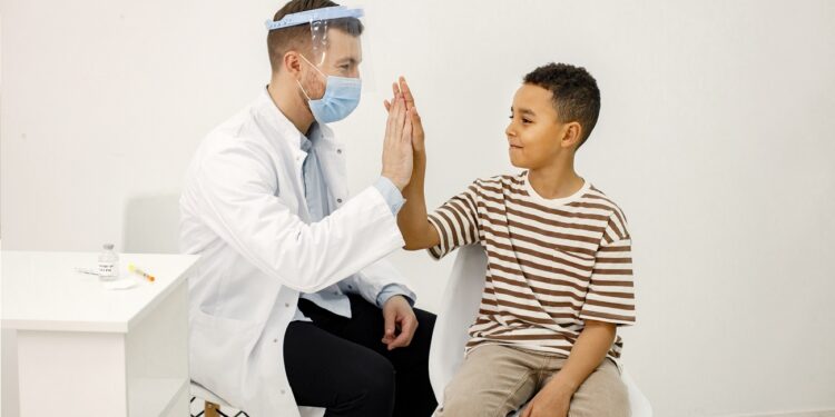 Male doctor sitting at table and wearing face mask. Man wearing white medical gown while isolated on white backgroun. Man give a high five to a little boy.