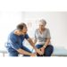 Photo of senior woman having some knee pain. She's at doctor's office having medical examination by a male doctor. The doctor is touching the sensitive area and trying to determine the cause of pain.