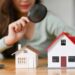 Woman looking at house models through magnifying glass. House selection, real estate appraisal and house search concept.