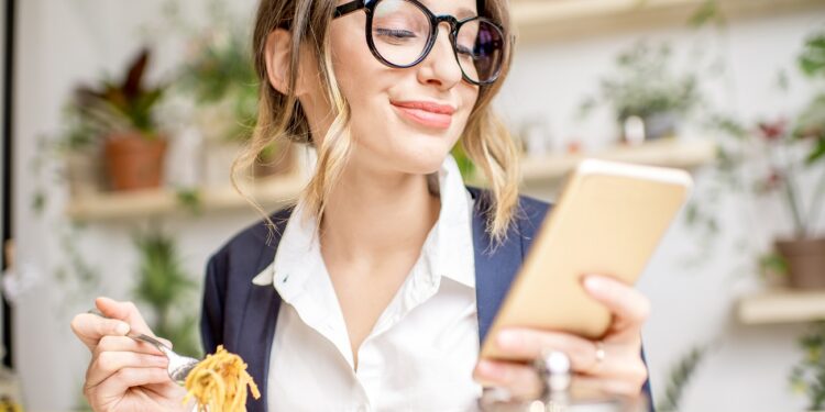 Businesswoman holding phone during the lunch with salad sitting at the vegan restaurant