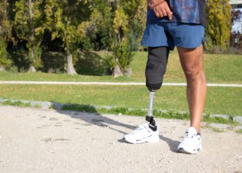 Close-up of Caucasian man with mechanical leg. Sportsman in blue shorts and white sneakers photographed in park. Sport, disability concept