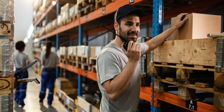 Happy dispatcher using walkie-talkie while working in distribution warehouse.