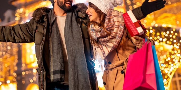 Beautiful young couple in love having fun doing Christmas shopping, walking down decorated city streets carrying shopping bags