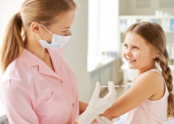 Adorable girl looking at nurse while she making her an injection in clinics