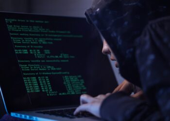 Computer hacker in hooded shirt typing software algorithms and stealing data from computer network on laptop.