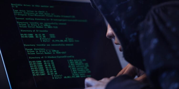 Computer hacker in hooded shirt typing software algorithms and stealing data from computer network on laptop.