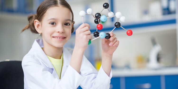 Girl scientist in lab coat holding molecular model and smiling at camera; Shutterstock ID 601069865; purchase_order: -; job: -; client: -; other: -