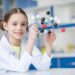 Girl scientist in lab coat holding molecular model and smiling at camera; Shutterstock ID 601069865; purchase_order: -; job: -; client: -; other: -