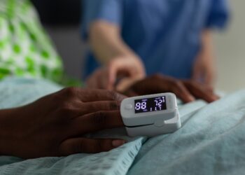 Closeup of african american sick patient resting in bed with medical oximeter on finger during clinical consultation in hospital ward. Woman nurse monitoring heartbeat rate. Medicine services