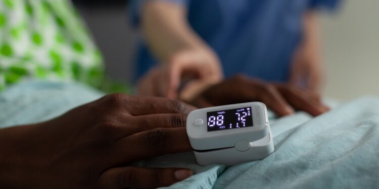 Closeup of african american sick patient resting in bed with medical oximeter on finger during clinical consultation in hospital ward. Woman nurse monitoring heartbeat rate. Medicine services