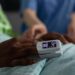 Closeup of african american sick patient resting in bed with medical oximeter on finger during clinical consultation in hospital ward. Woman nurse monitoring heartbeat rate. Medicine services