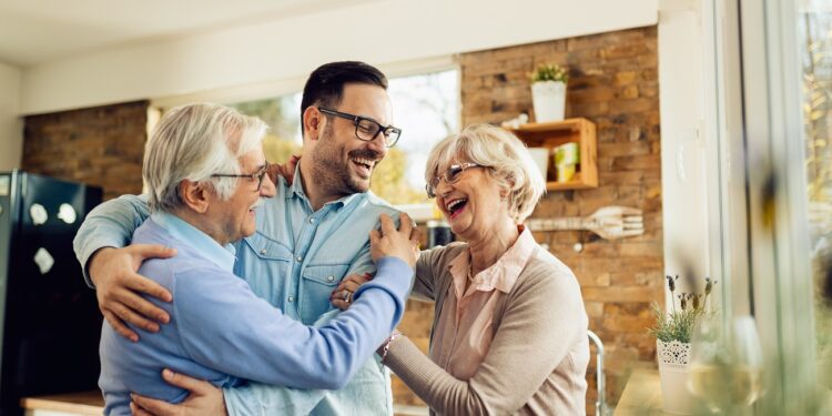 Happy mature parents having fun while embracing their adult son who came to visit them at home.