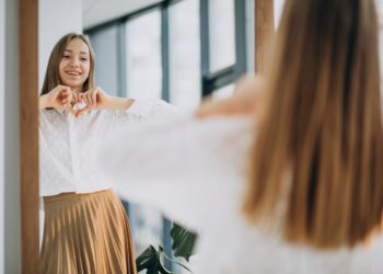 Pretty young woman in casual outfit looking into mirror