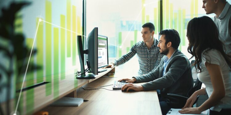 Closeup side view of group of young IT experts completing a task, a part of their daily routine at IT company. There are three men and a woman.