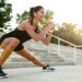 Portrait of a smiling fitness woman in earphones doing stretching exercises on stairs outdoors