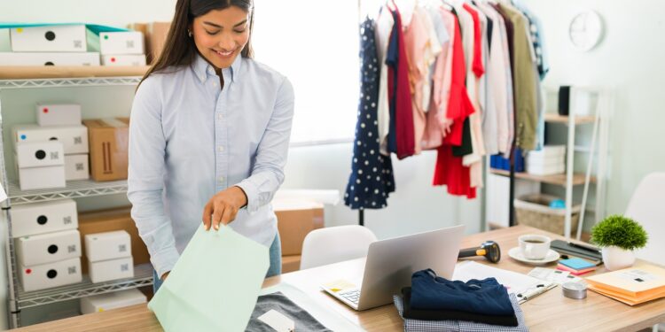I got a new online order from a client. Happy female entrepreneur smiling while preparing to ship a package from her fashion clothing shop