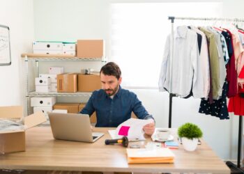 Focused business owner sitting at his office desk and updating the products and new fashion clothes on his online e-commerce