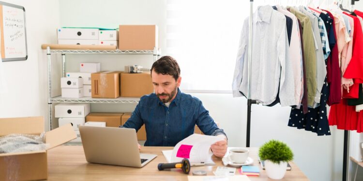 Focused business owner sitting at his office desk and updating the products and new fashion clothes on his online e-commerce