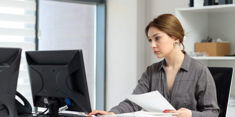 a front view young beautiful lady in grey shirt working with the documents and laptop sitting inside her office during daytime building job activity