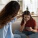 Supportive mother comforting sad teenage girl rejected by friends, helping depressed teen daughter to deal with breakup. Upset depressed adolescent child looking at phone at home, waiting for call