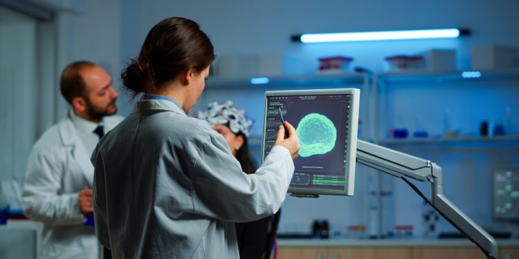 Researcher looking at monitor analysing brain scan while coworker discussing with patient in background about side effects, mind functions, nervous system, tomography scan working in laboratory