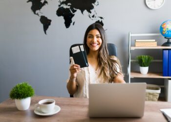 I am here to help you with your booking and travel questions. Female sales agent holding plane tickets while smiling and making eye contact at the travel agency