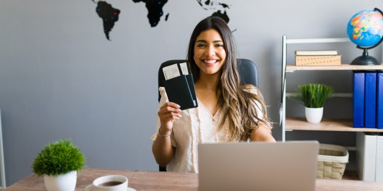 I am here to help you with your booking and travel questions. Female sales agent holding plane tickets while smiling and making eye contact at the travel agency