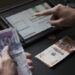 Male had holding colombian banknotes while he does the math on a tablet