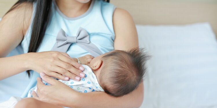 Mother breast feeding and holding hand of her baby.