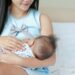 Mother breast feeding and holding hand of her baby.