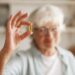 Food, nutrition, diet and health concept. Close up shot of elderly woman's hand holding fish oil or omega-3 polyunsaturated fatty acid supplement in shape of capsule, going to take one during lunch