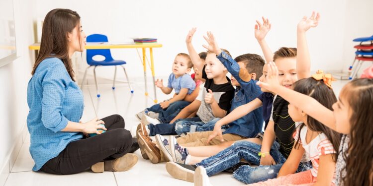 Profile view of a group of preschool students raising their hands and trying to participate at school