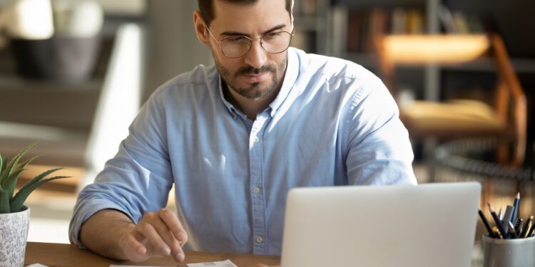 Focused young Caucasian man look at laptop screen calculate expenses expenditures pay bills taxes online. Millennial male busy managing household family budget, take care of financial paperwork.; Shutterstock ID 1817934827; ordering_party: -; job_project: -; purchase_order: -; other: -