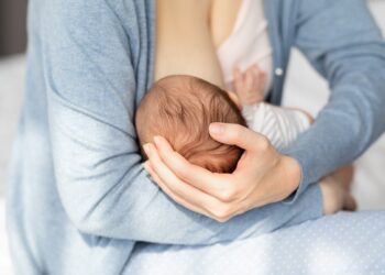 Lactation Concept. Closeup Shot Of Unrecognizable Woman Breastfeeding Newborn Baby At Home, Supporting His Head With Hand, Infant Child Eating Mom's Breast Milk, Cropped Image