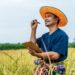 Asian middle aged farmer man wearing straw hat write on clipboard in rice field with smile during keep data with Smart farming Agriculture technology and organic agriculture