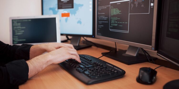 The young dangerous hacker breaks down government services by downloading sensitive data and activating viruses. A man uses a laptop computer with many monitors.