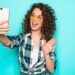 Portrait of beautiful smiling model with afro curls hairstyle dressed in summer hipster clothes.Sexy carefree girl posing in studio near blue wall.Trendy funny and positive woman makes selfie