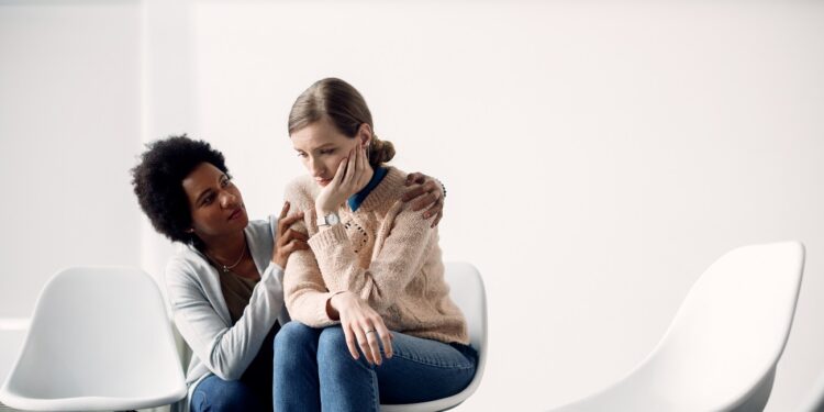 Young distraught woman being consoled by African American woman at community center. Copy space.