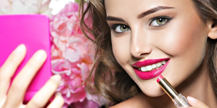 Smiling Woman applying lipstick. Beautiful girl makes makeup