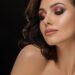 Beautiful model with long eyelashes, plump lips and glowing eye shadow posing at camera. Sensual, perfect, pretty, lady with seductive naked shoulders, perfect skin.