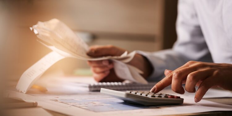 Close-up of economist using calculator while going through bills and taxes in the office.