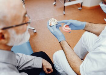 Handsome old man talking to the dendist. Two men in the dentist's office. The doctor shows the patient dentures