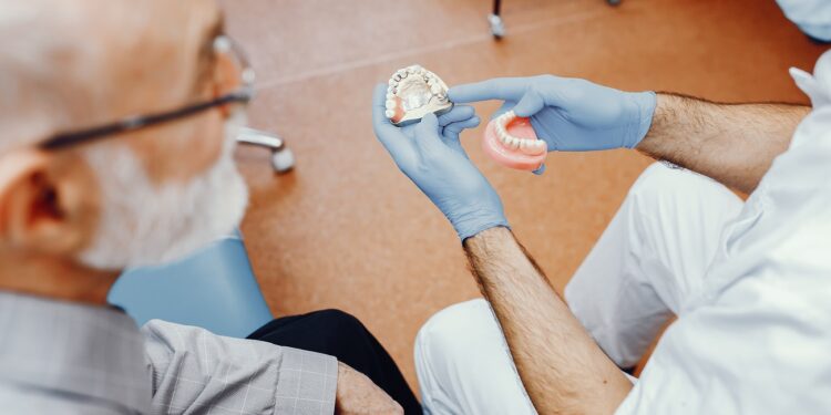 Handsome old man talking to the dendist. Two men in the dentist's office. The doctor shows the patient dentures