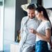 smiling couple using smartphone together in kitchen, smart home concept