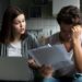 Angry wife scolding blaming upset husband of unpaid bills, bankruptcy or past due debt, unhappy millennial couple having financial problems arguing at home sitting on sofa with laptop and papers