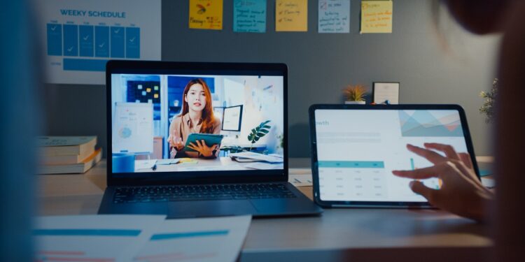 Young Asia financial student ladies watching lesson online and studying with laptop and tablet in living room from home at night. Taking notes while looking at computer screen, Learn online concept.