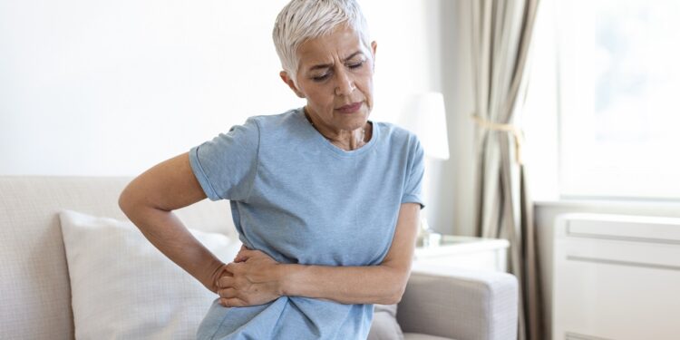 Unhealthy mature woman holding belly, feeling discomfort, health problem concept, unhappy older female sitting on bed, suffering from stomachache, food poisoning, gastritis, abdominal pain, climax