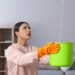 Young woman collecting leaking water from ceiling at home. Time to call roof repair service
