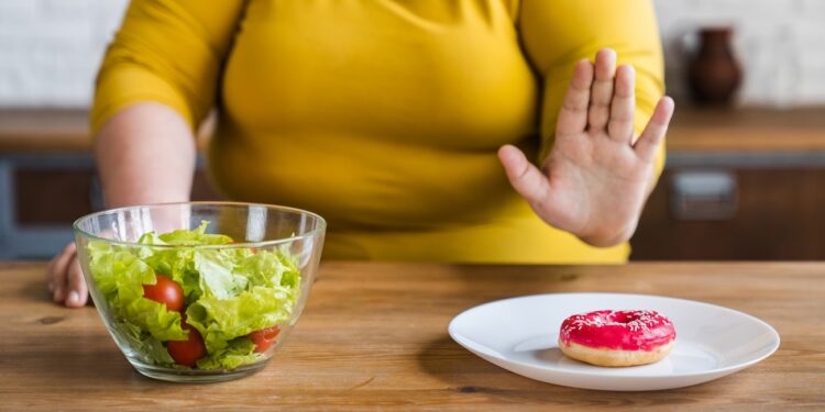 Pensive fat chubby obese caucasian woman opting for healthy food instead of sweets. Dieting concept. Hard choice between healthy lifestyle and bad eating habits.